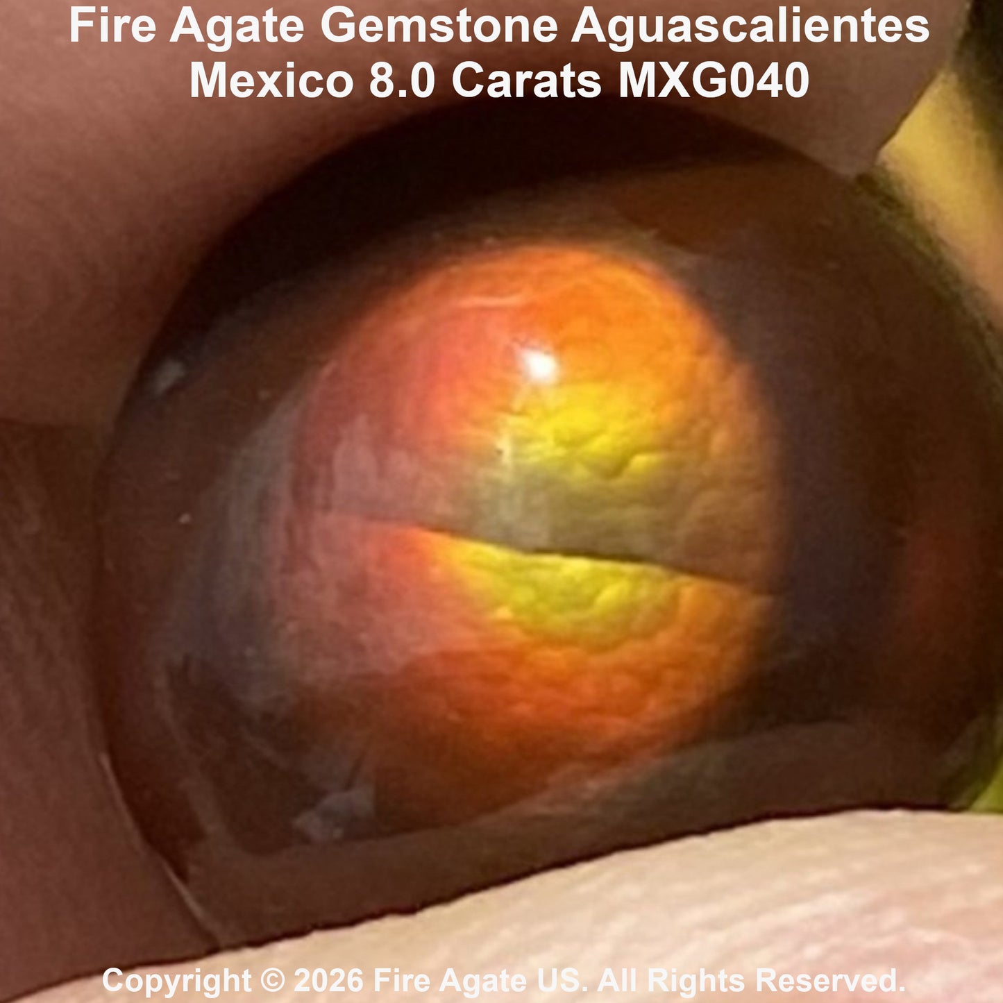 A close-up of a round fire agate gemstone with a prominent orange and yellow band, held between fingers.