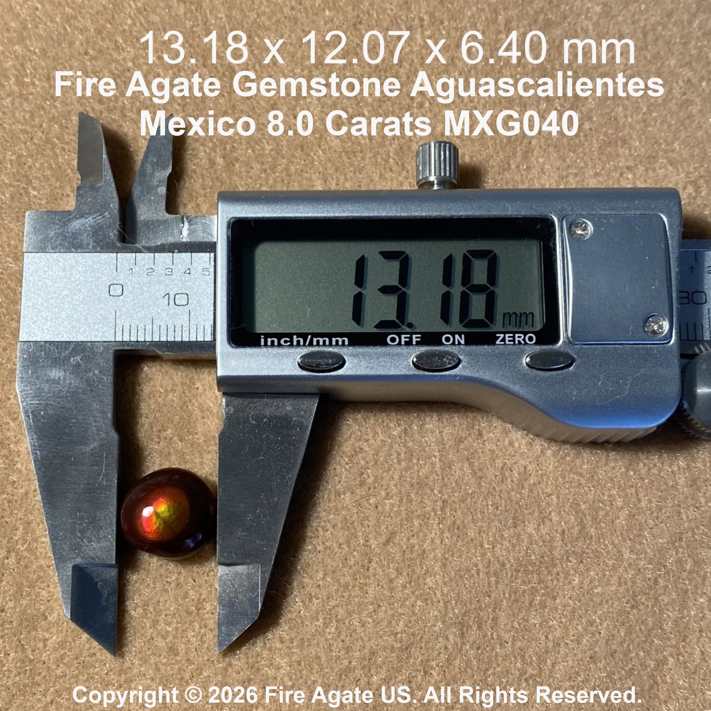 A small round fire agate gemstone with a reddish brown body and green iridescent edges, shown next to a digital caliper displaying 13.18 mm.