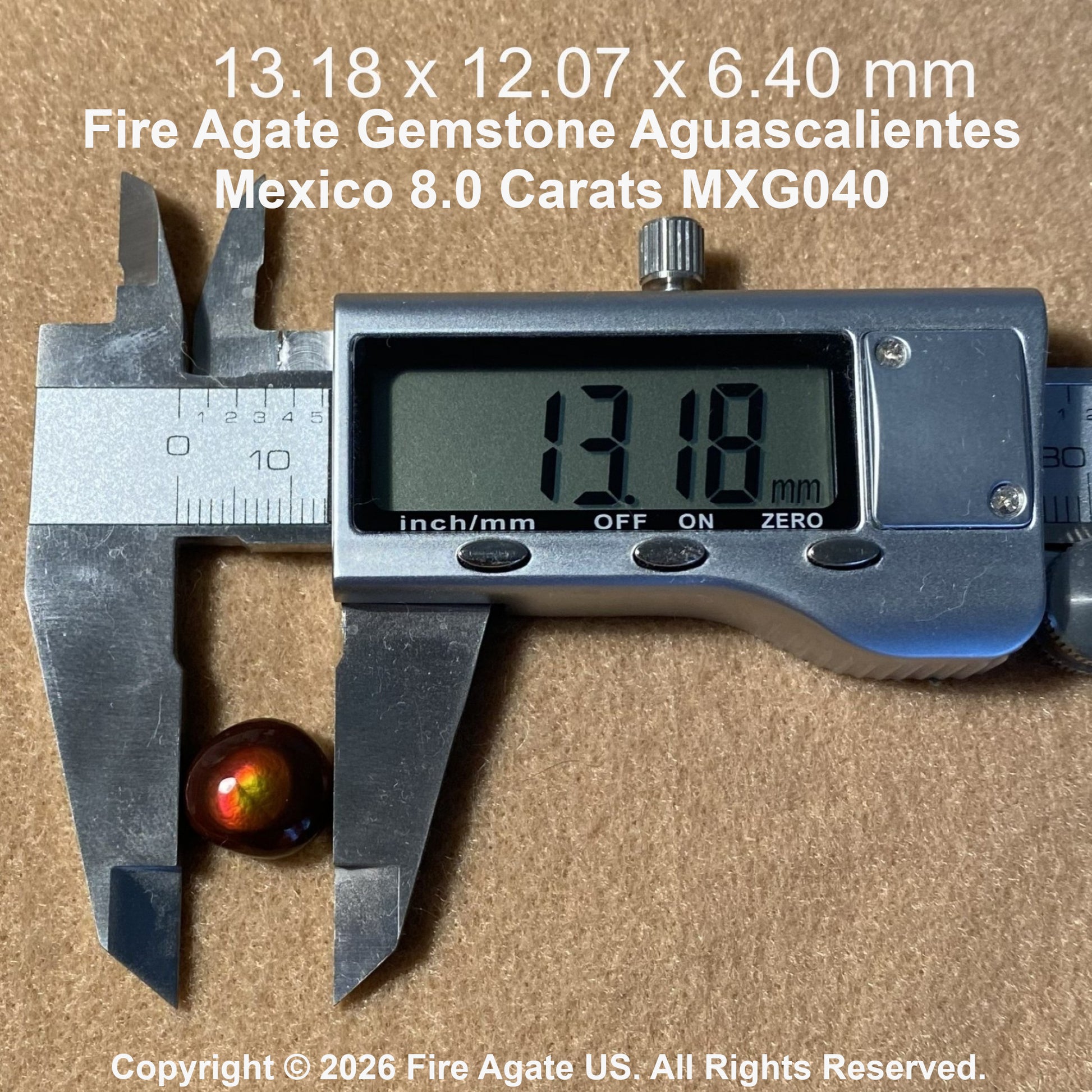 A small round fire agate gemstone with a reddish brown body and green iridescent edges, shown next to a digital caliper displaying 13.18 mm.