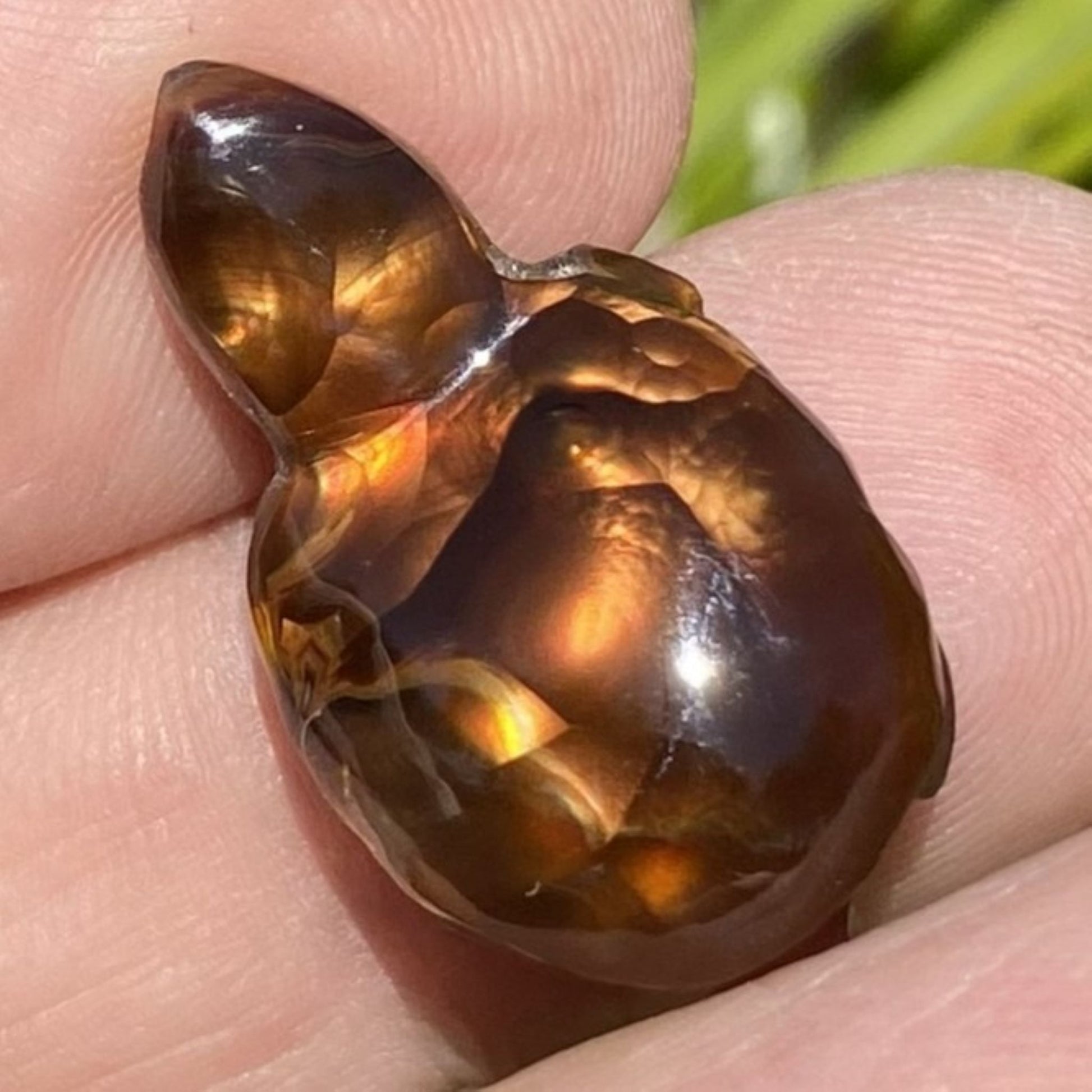 Aguascalientes Fire Agate Creature Carving Charm Specimen gemstone held between fingers with a blurred natural background