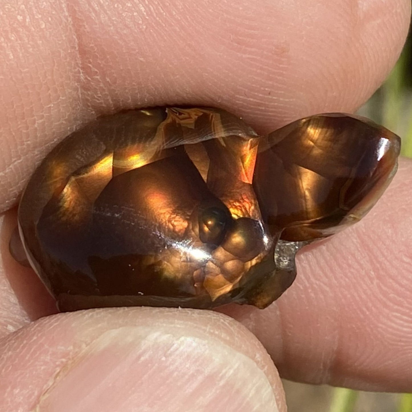 Close-up of a hand holding a polished Aguascalientes Fire Agate Creature Carving Charm Specimen with a wavy pattern.