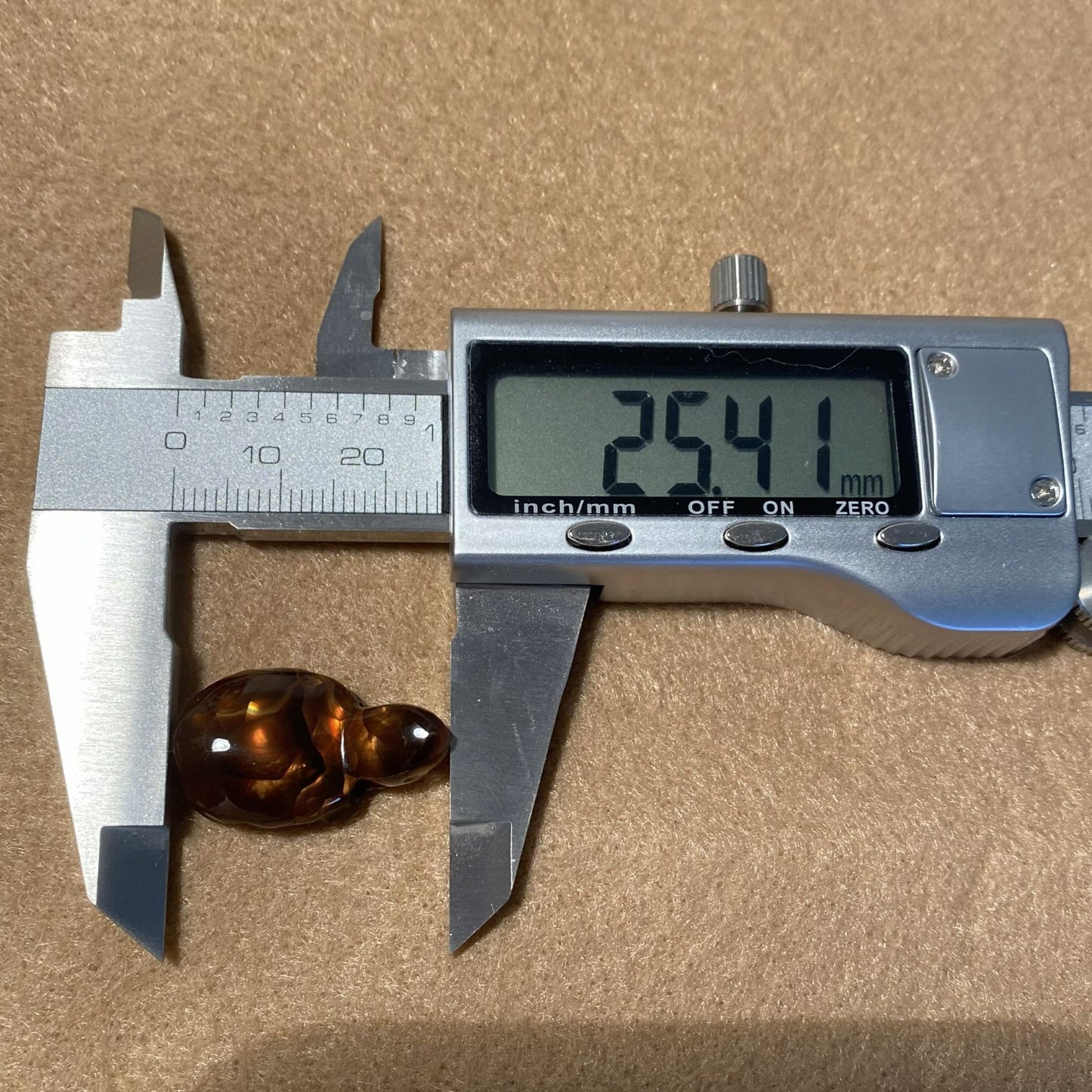 Digital caliper measuring a small amber-colored object on a brown background