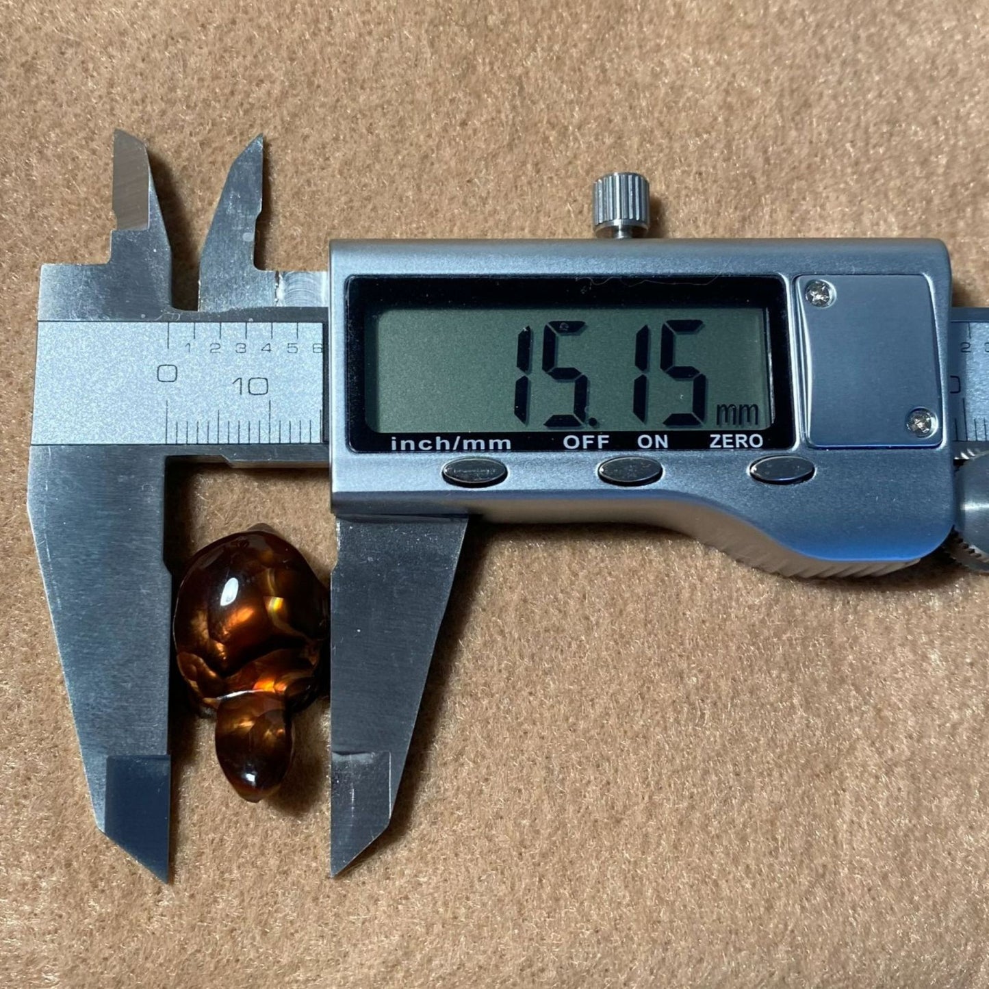 Digital caliper measuring an Aguascalientes Fire Agate Creature Carving Charm Specimen on a brown background