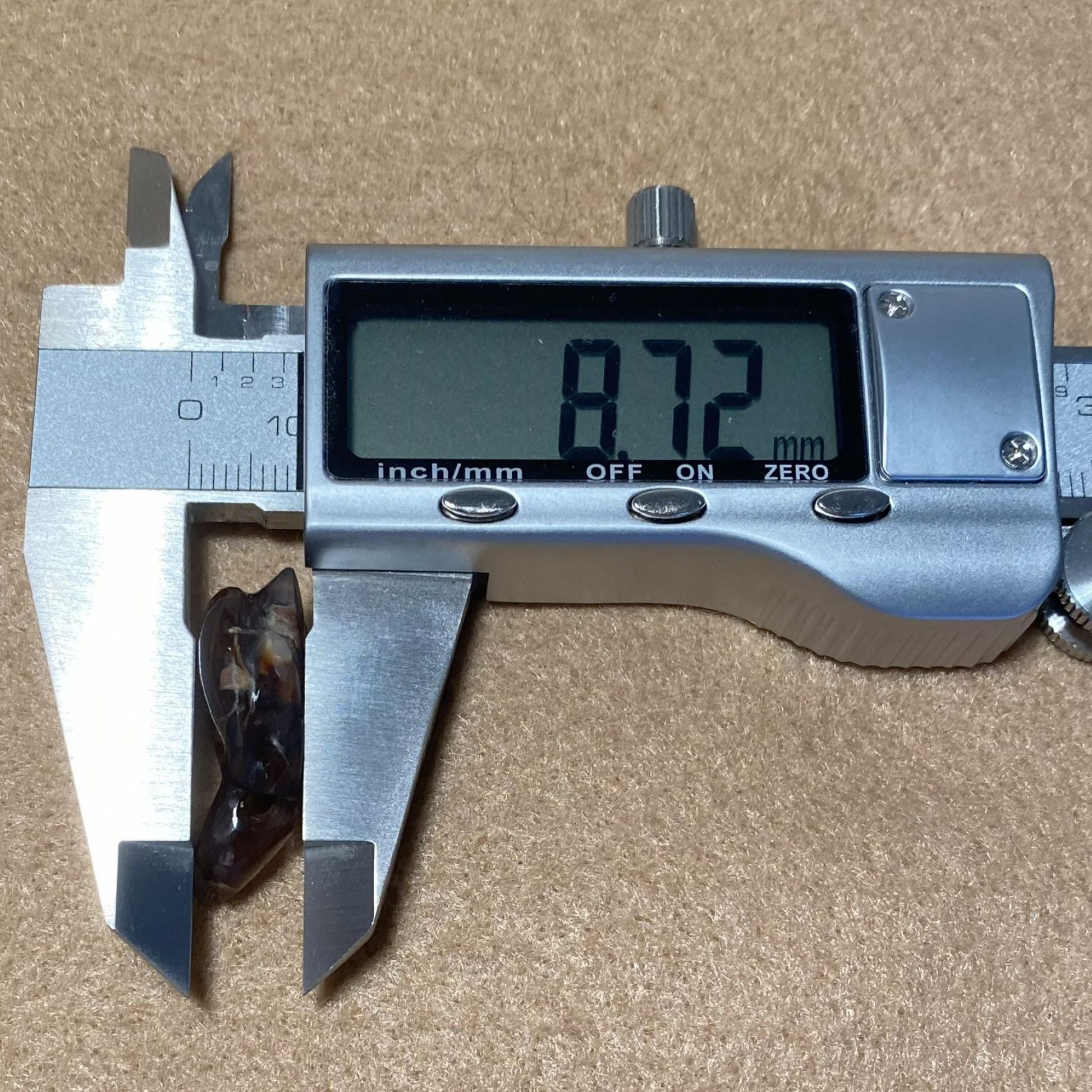 Digital caliper measuring a small object with a displayed measurement on a brown background