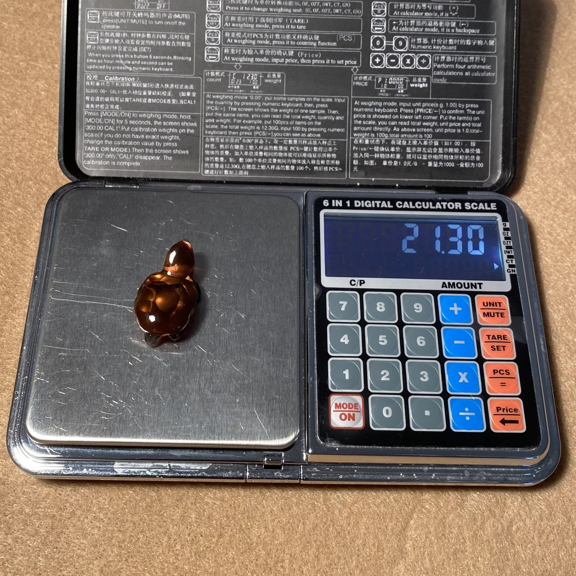 Digital calculator scale with a small fire agate carving on it, displaying a weight reading.
