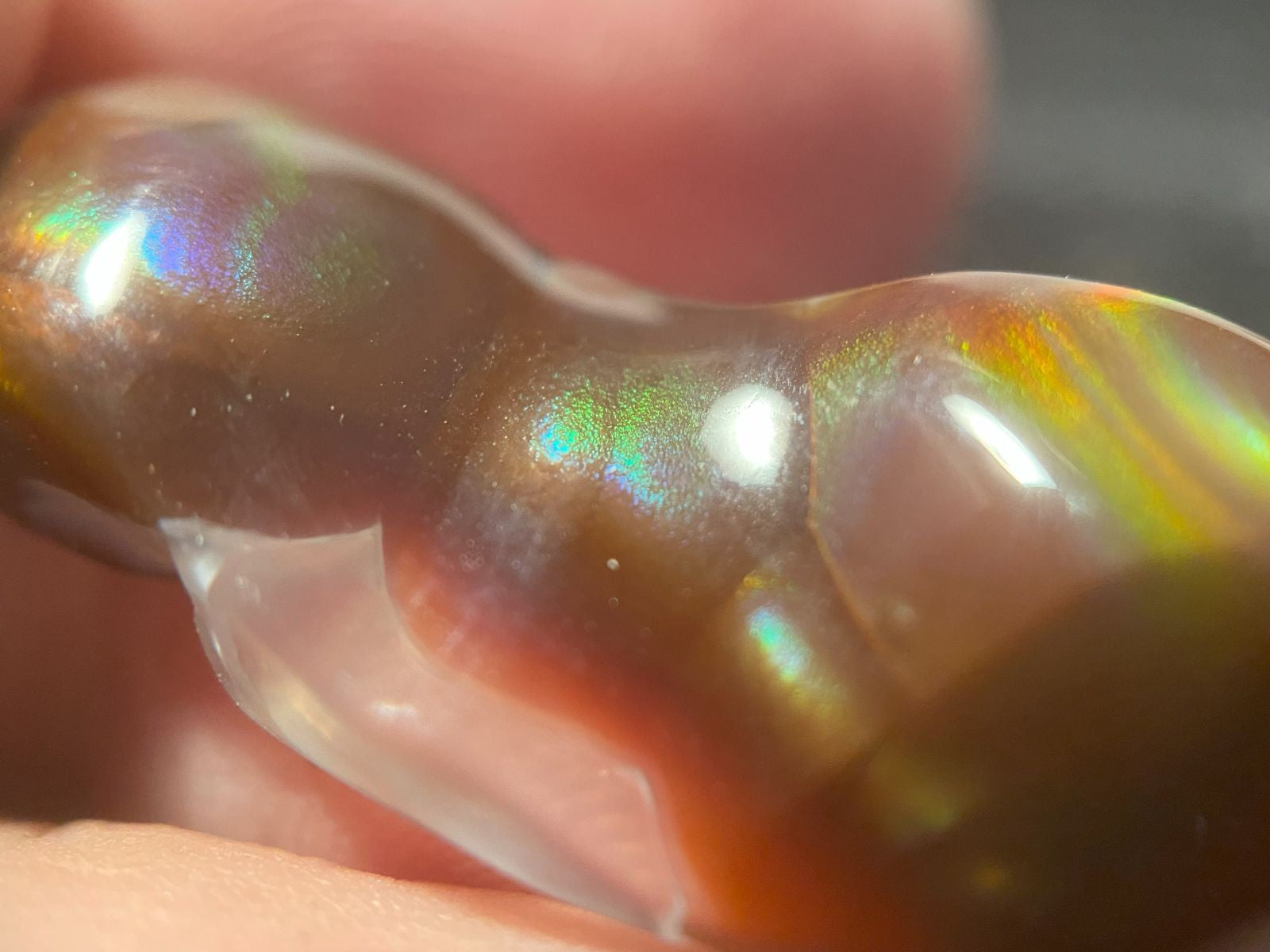 Close-up of a rainbow-colored Aguascalientes fire agate gemstone held between fingers