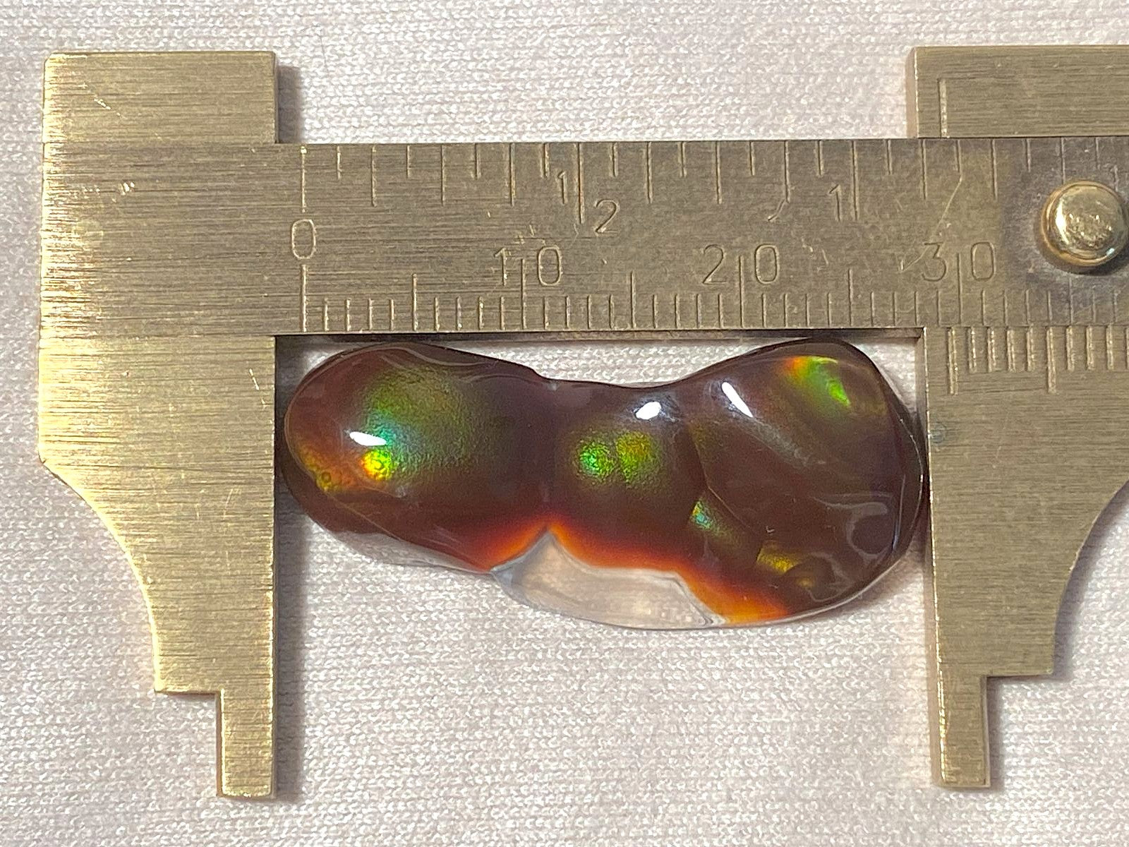 Aguascalientes fire agate gemstone with a measuring tool showing its dimensions on a light background