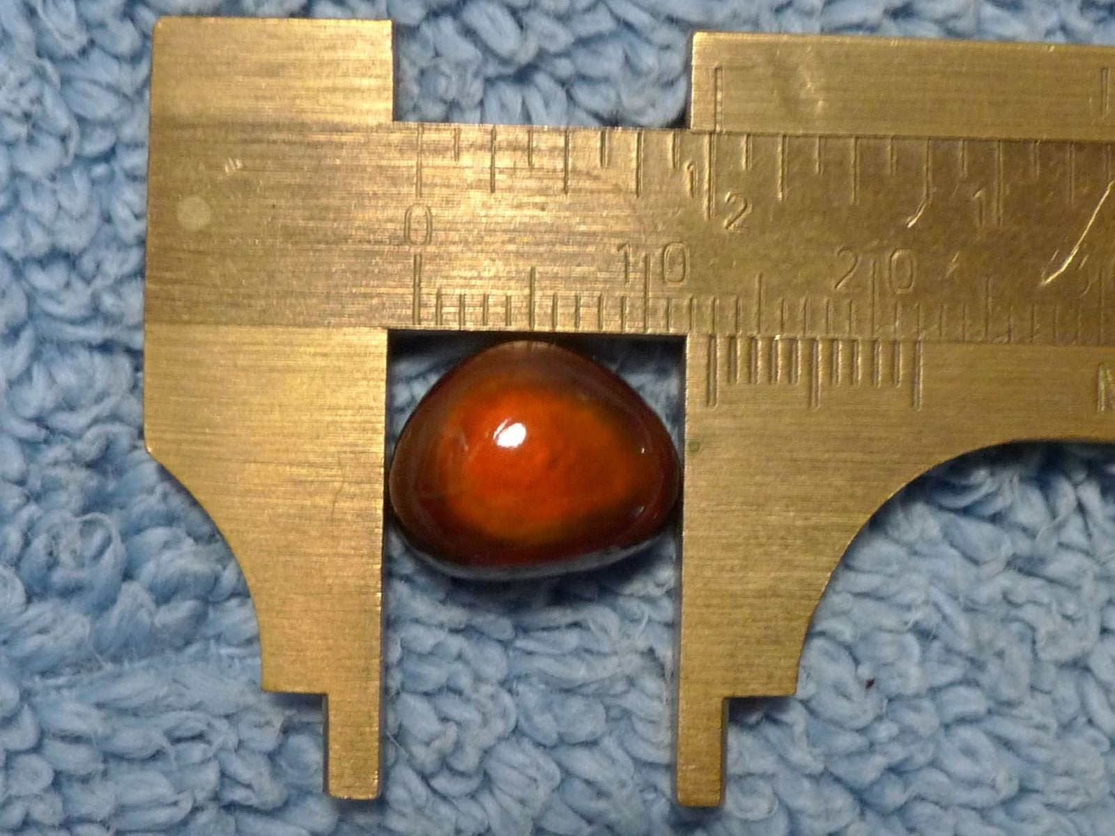 Gold-colored caliper measuring a red-orange gemstone on a blue textured background
