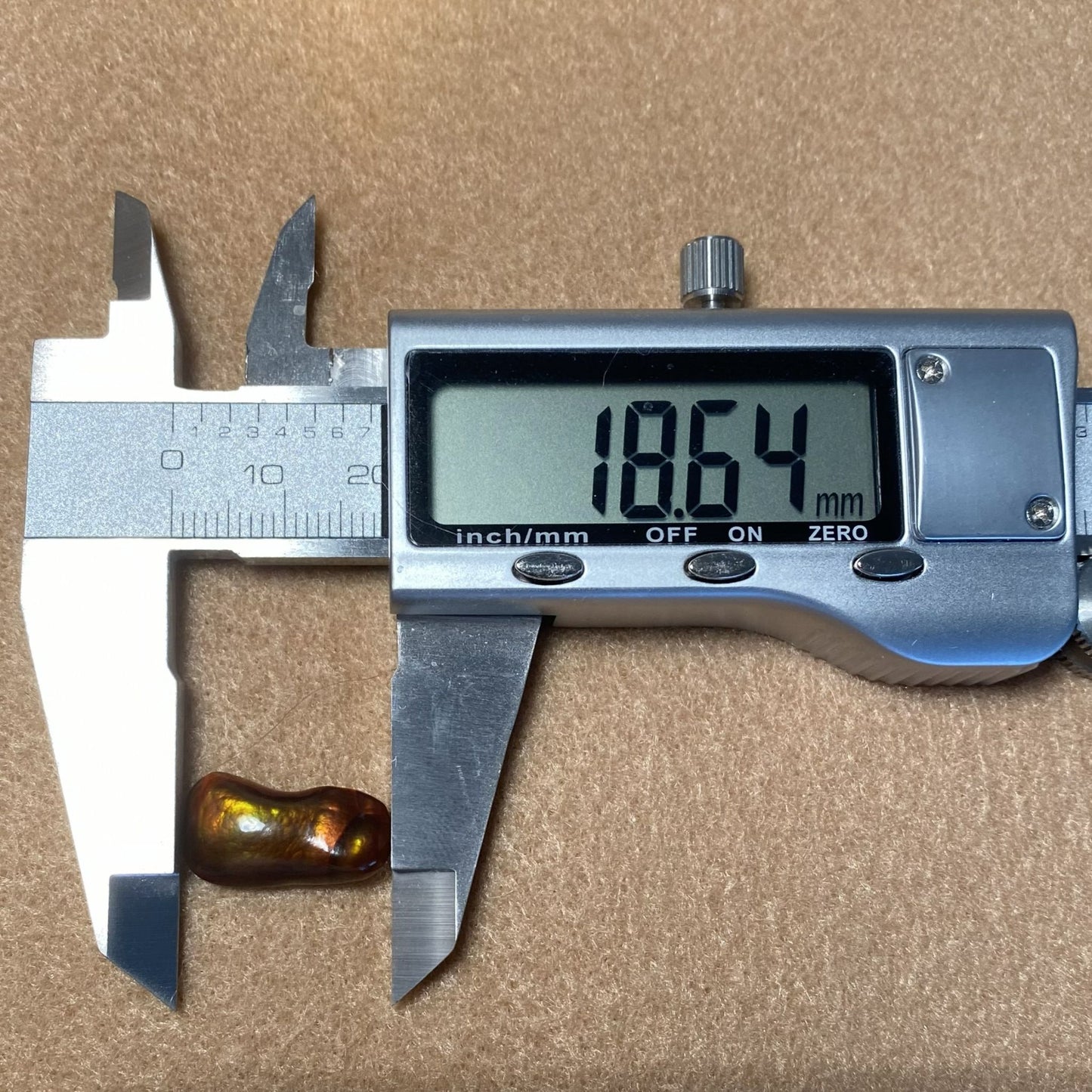 Digital caliper measuring a Slaughter Mountain Fire Agate Gemstone against a brown background