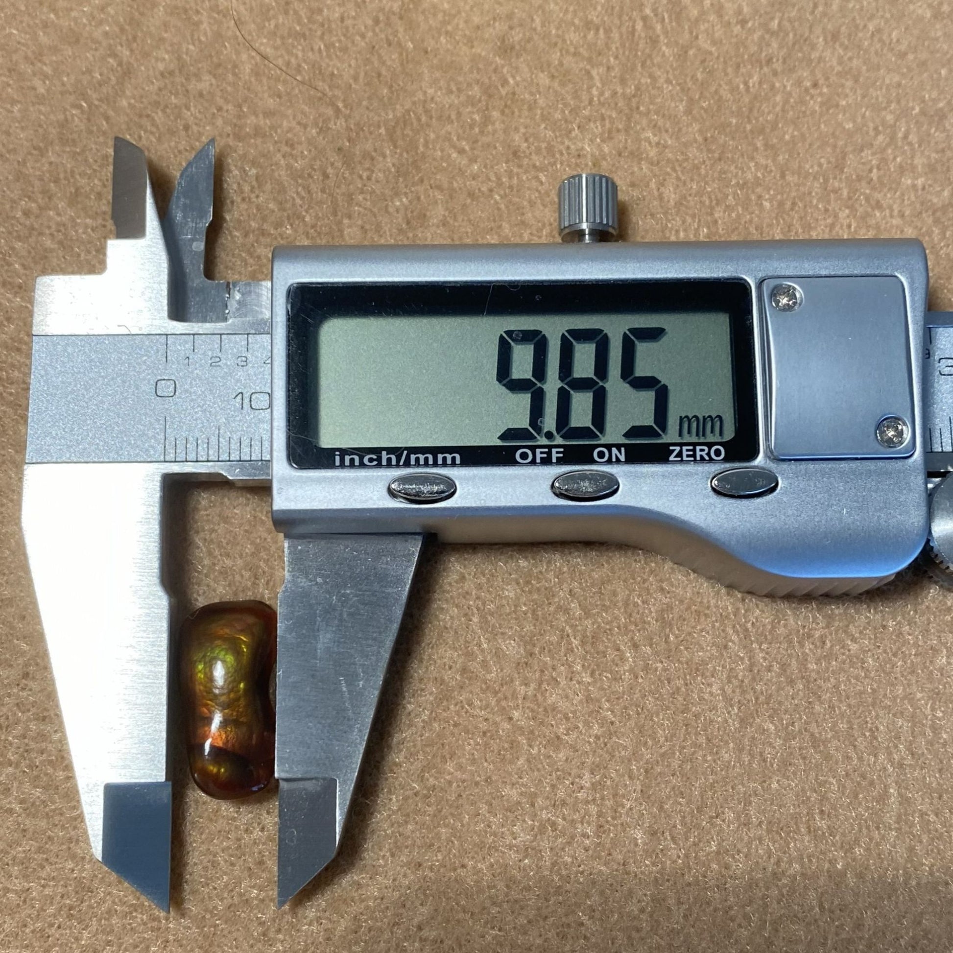 Digital caliper measuring a Slaughter Mountain Fire Agate Gemstone with a brown background