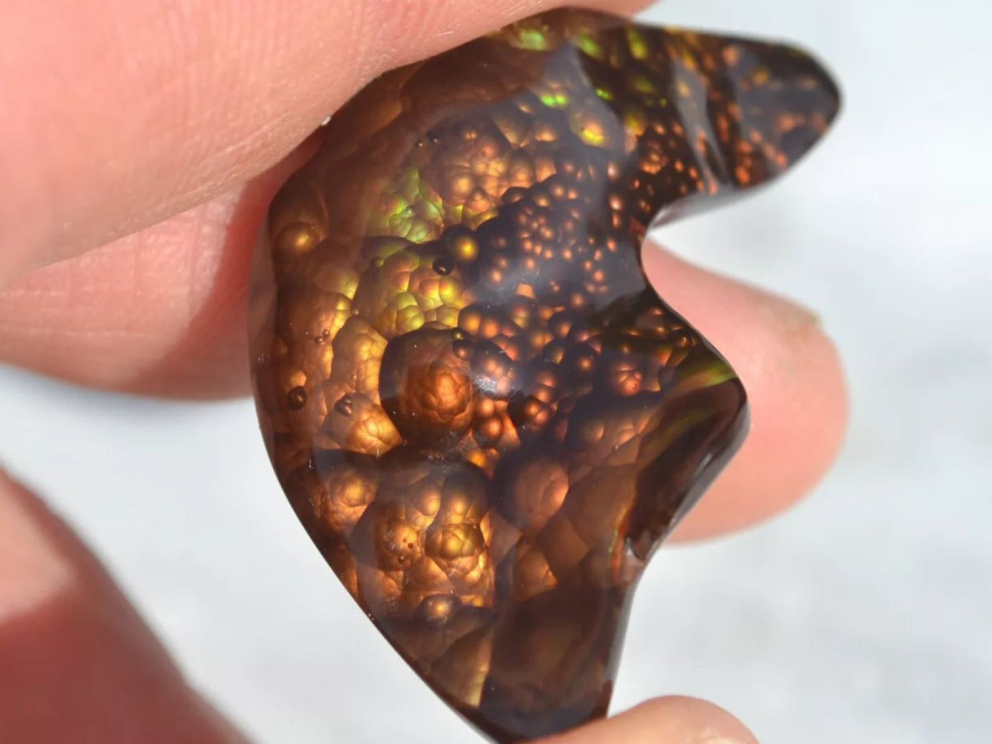 Close-up of a person holding a polished Slaughter Mountain fire agate gemstone with intricate patterns.