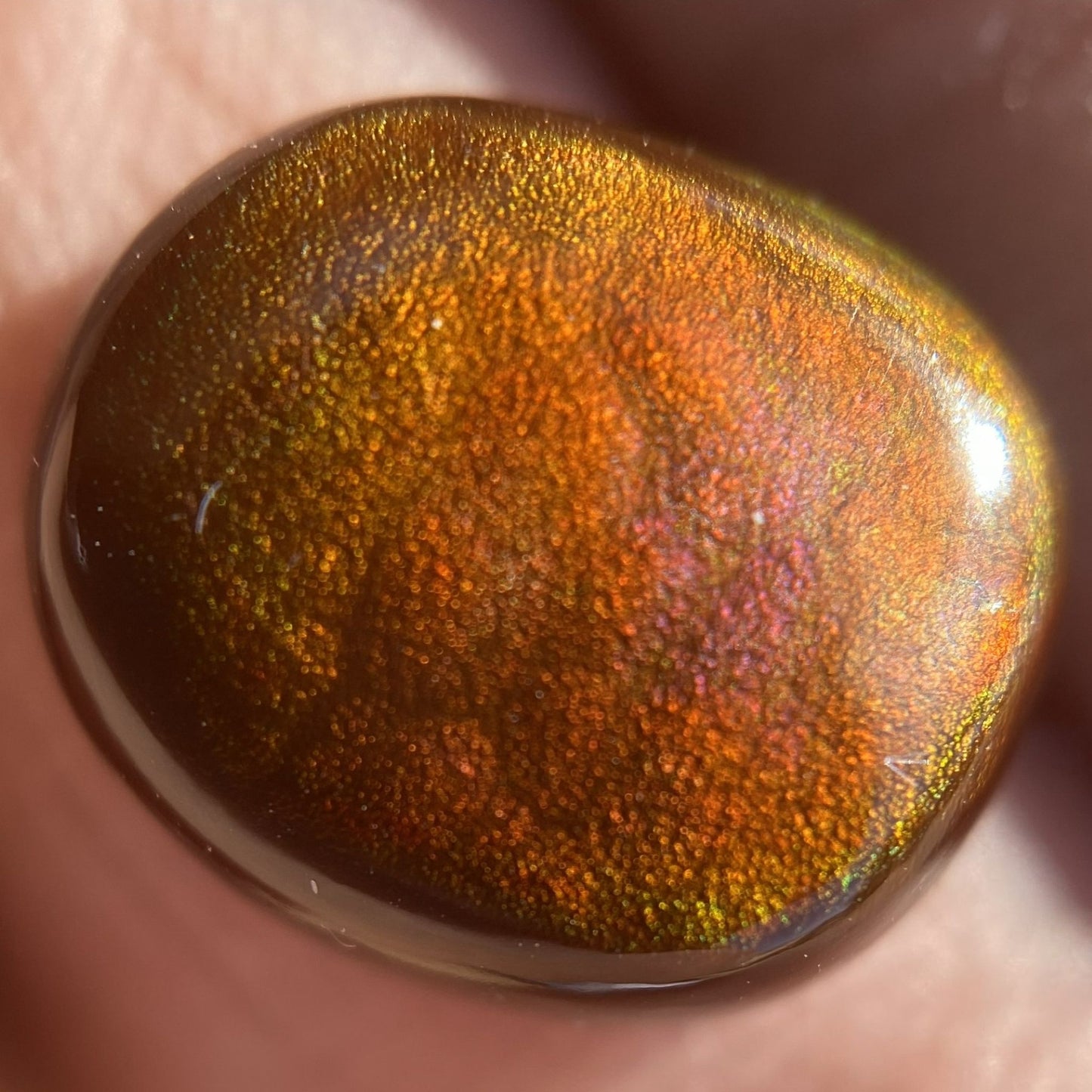 Close-up of a metallic fiery Slaughter Mountain fire agate gemstone held between fingers