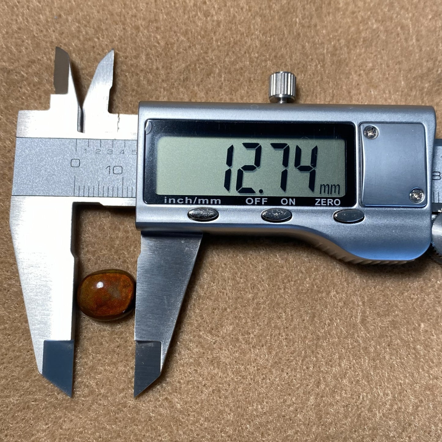 Digital caliper measuring a round fire agate with a brown background