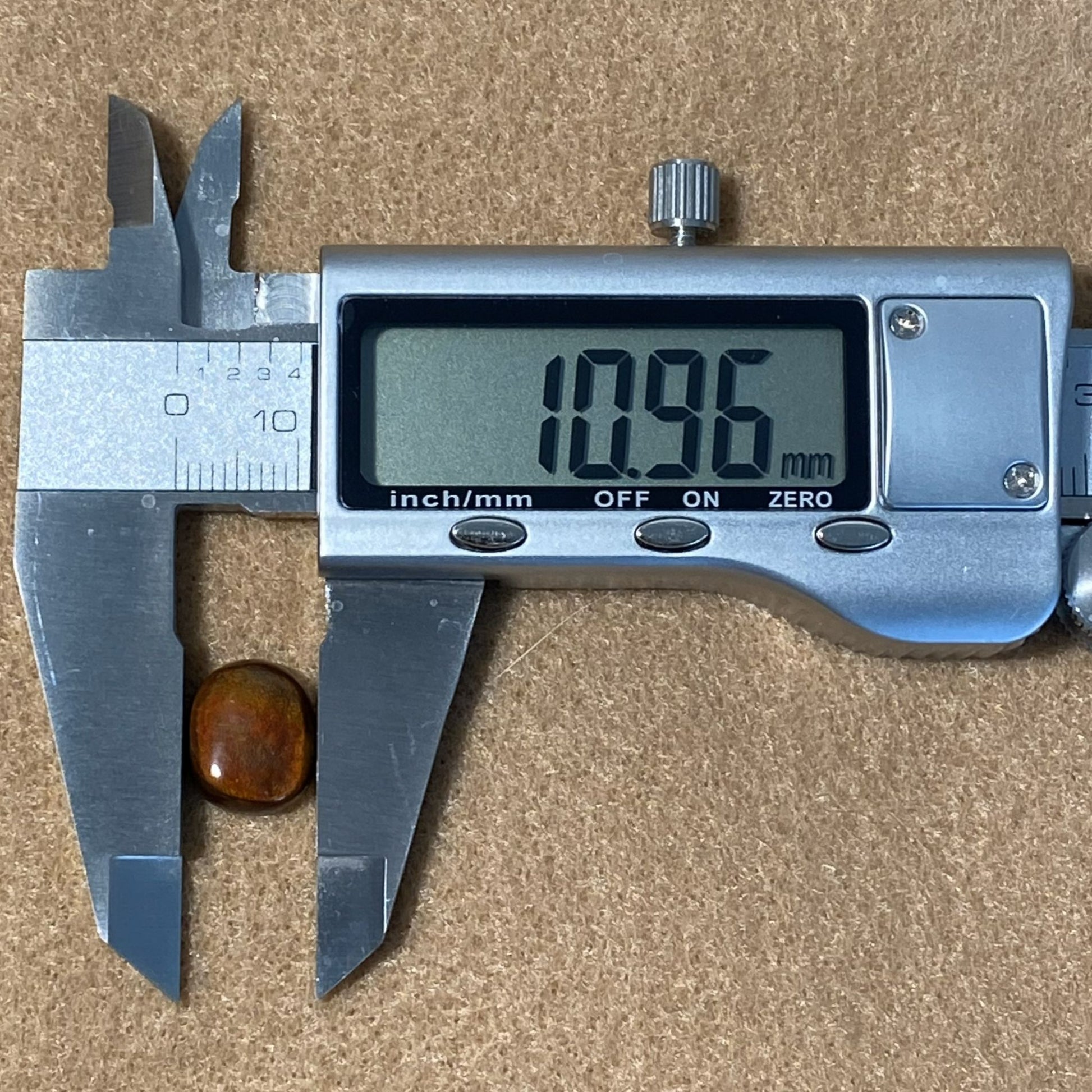 Digital caliper measuring a small round Slaughter Mountain fire agate gemstone on a brown background