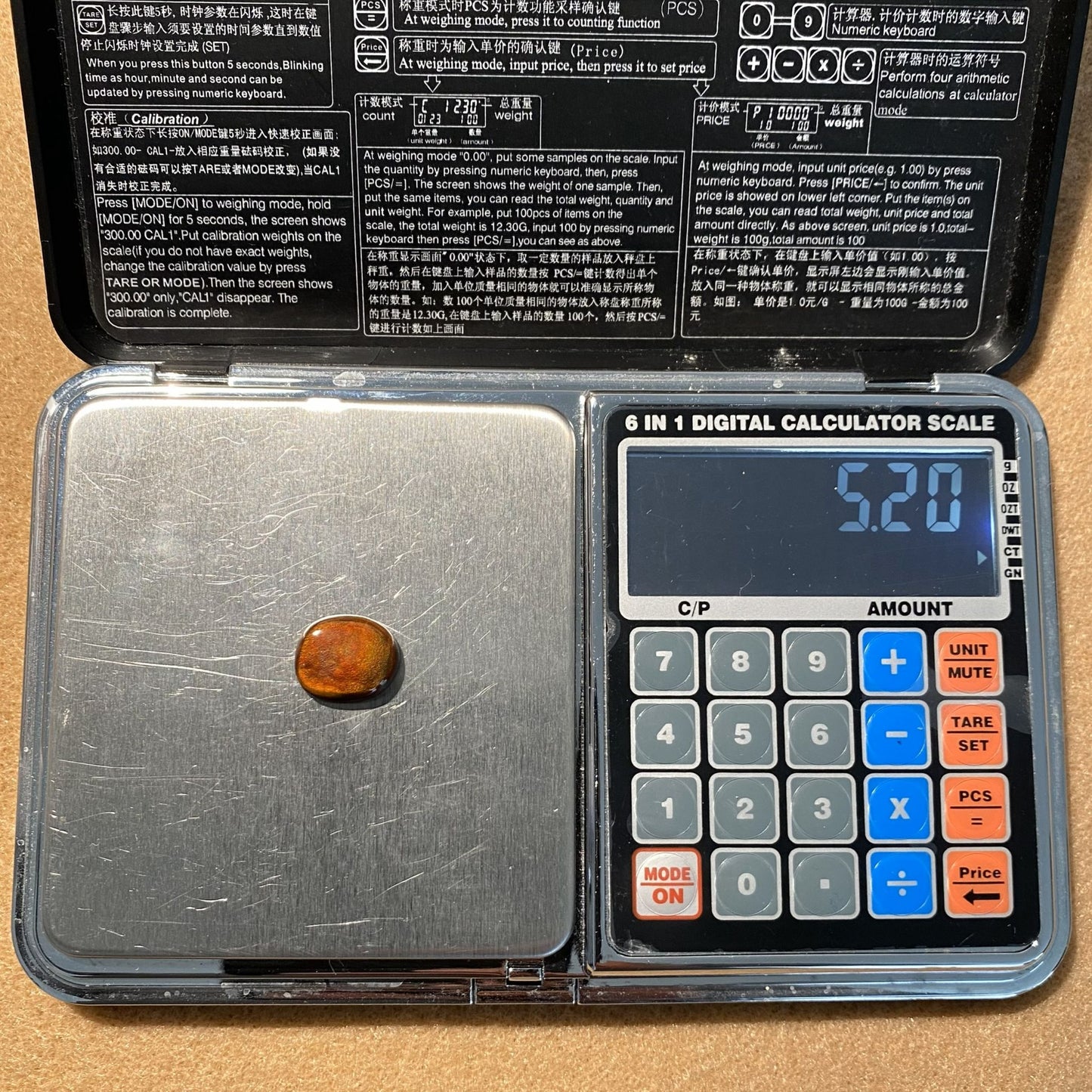 Digital calculator scale with a fire agate gemstone on it, showing a weight reading of 5.2 carats.