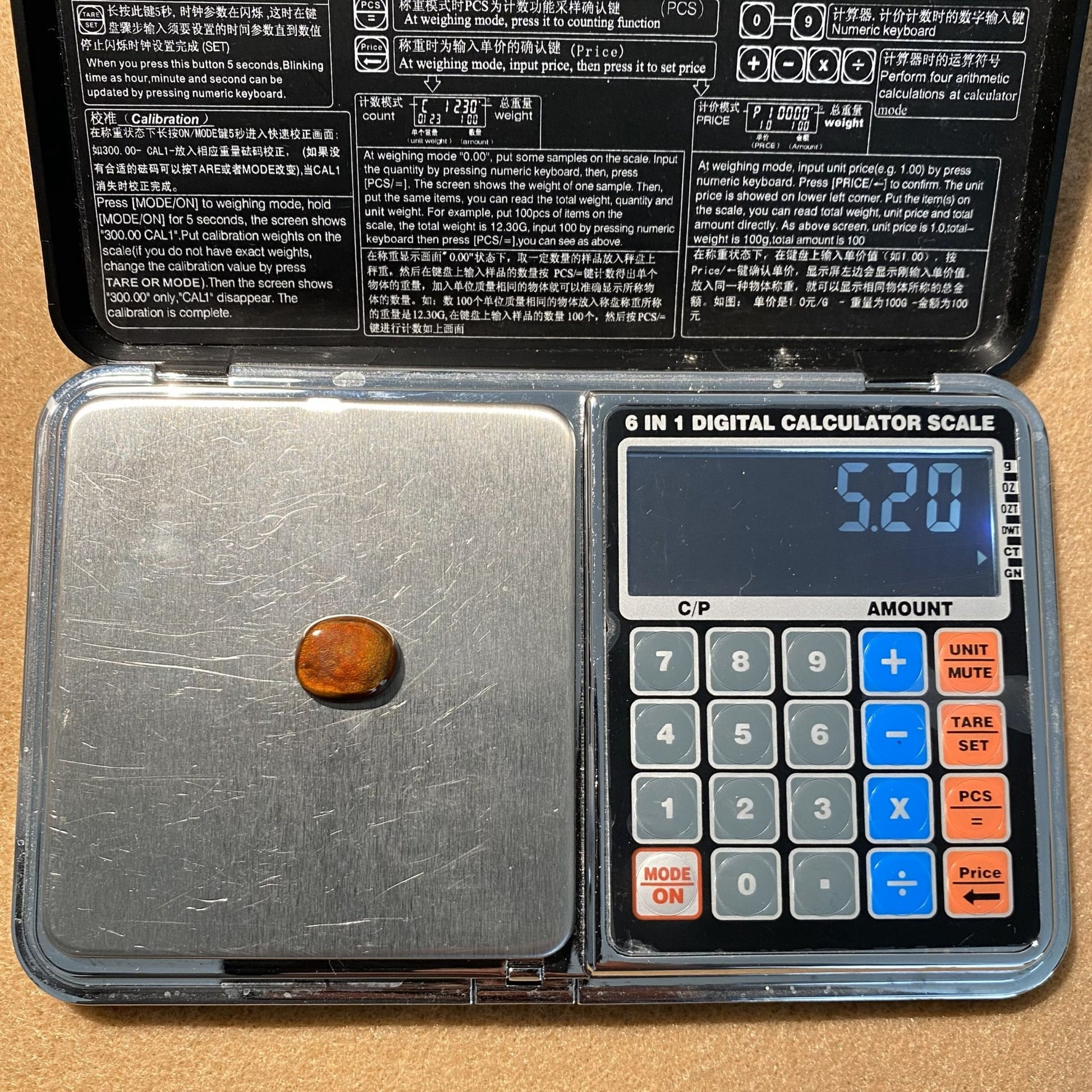 Digital calculator scale with a fire agate gemstone on it, showing a weight reading of 5.2 carats.