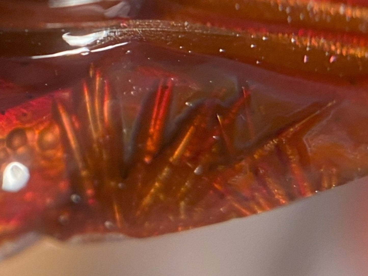 Close-up of a red and orange fire agate gemstone with saganite spikes on a white background