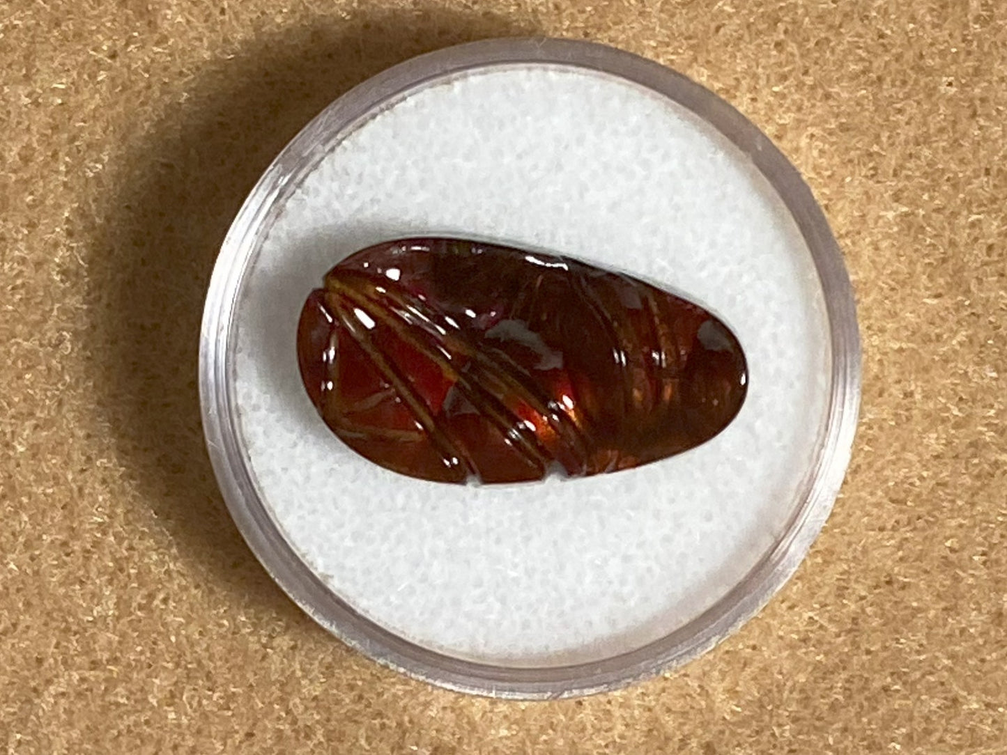 Brown fire agate gemstone in a clear container on a beige background