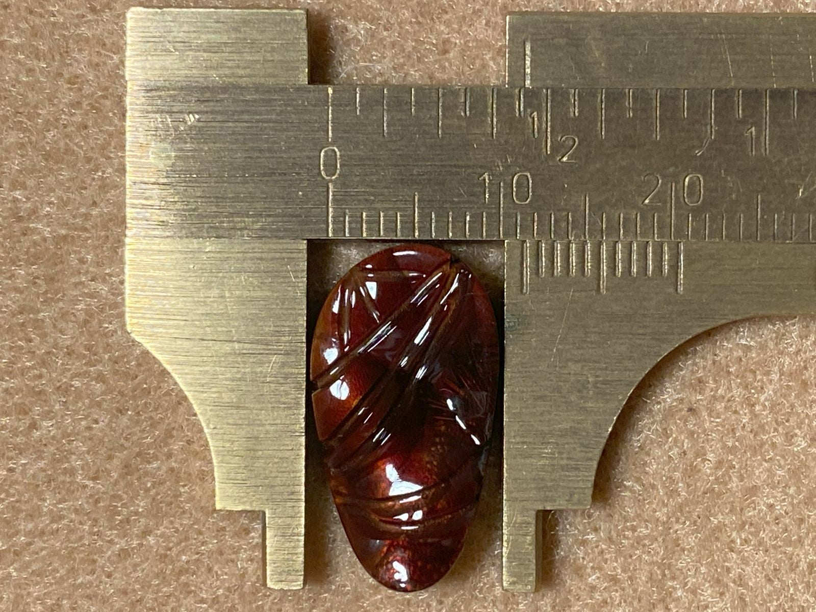 Brown fire agate gemstonet being measured with a ruler on a brown background