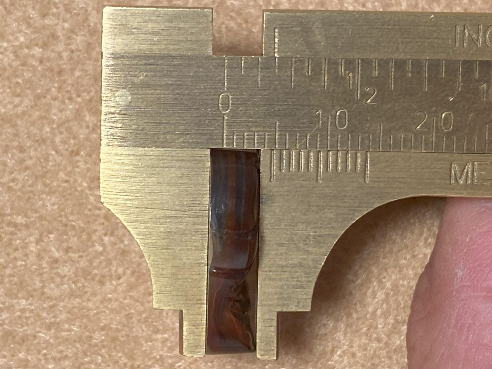 Brass vernier caliper measuring a small fire agate gemstone on a brown surface