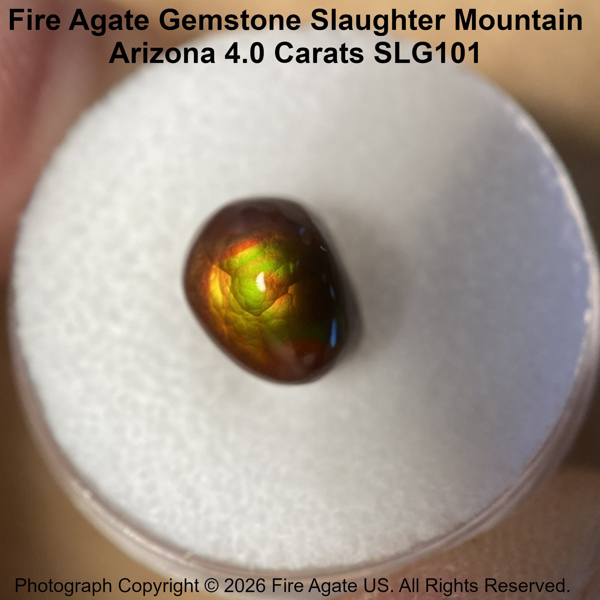 A 4.0 carat fire agate gemstone with a vibrant green, orange, and brown iridescent play-of-color, displayed on a white foam ring.
