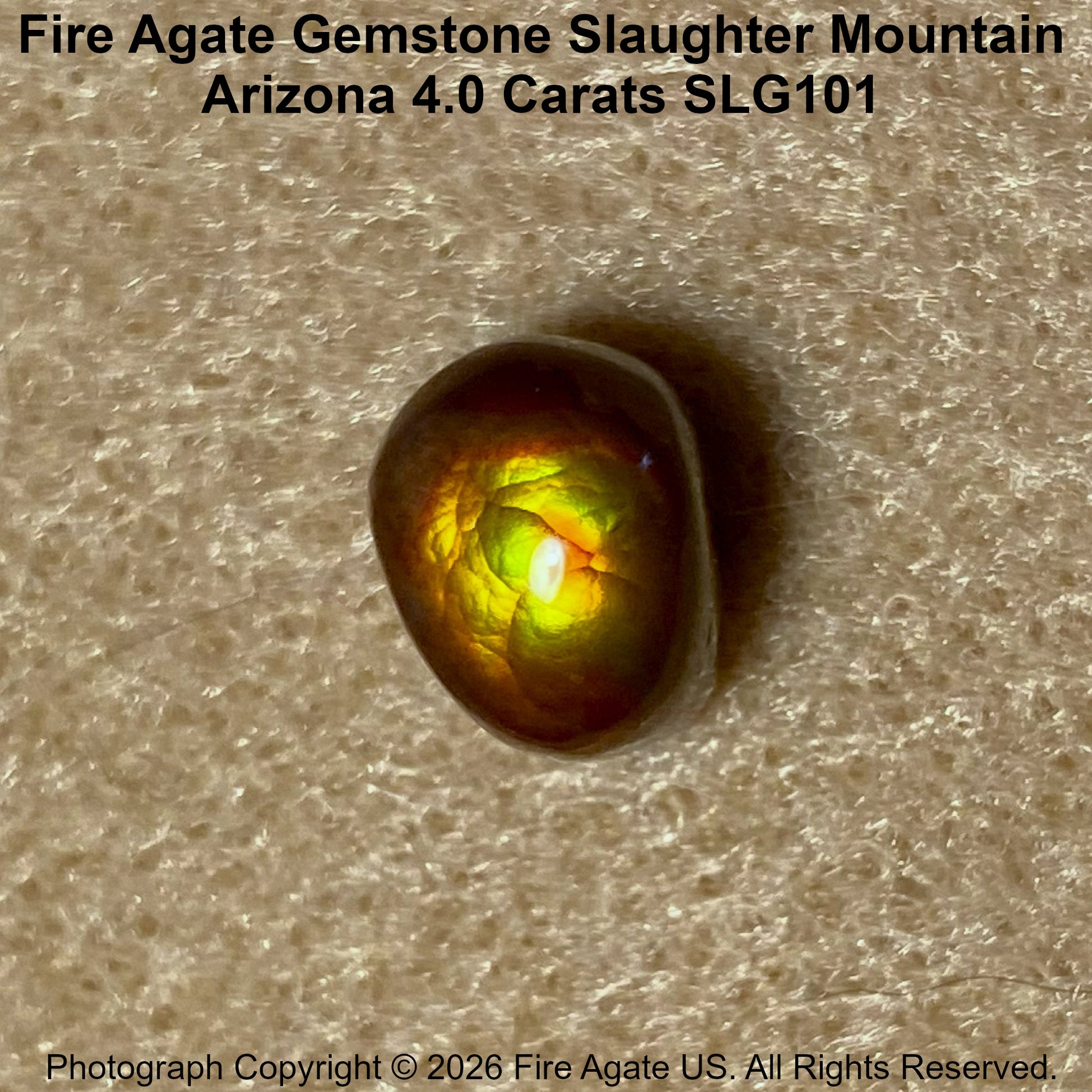 A polished Fire Agate gemstone with a vibrant green and yellow iridescent play-of-color, resting on a textured beige surface. Text overlays identify the variety as 'Slaughter Mountain' from Arizona.