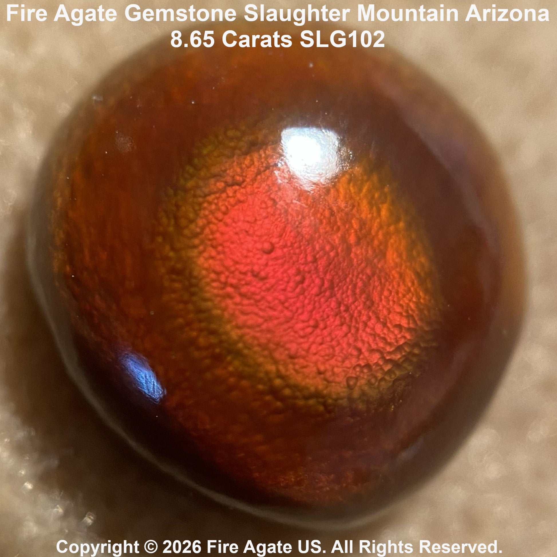 A polished fire agate gemstone with a vibrant red fiery pattern, photographed close-up on a neutral textured surface. Text overlays identify the stone as 'Fire Agate Gemstone Slaughter Mountain Arizona'.