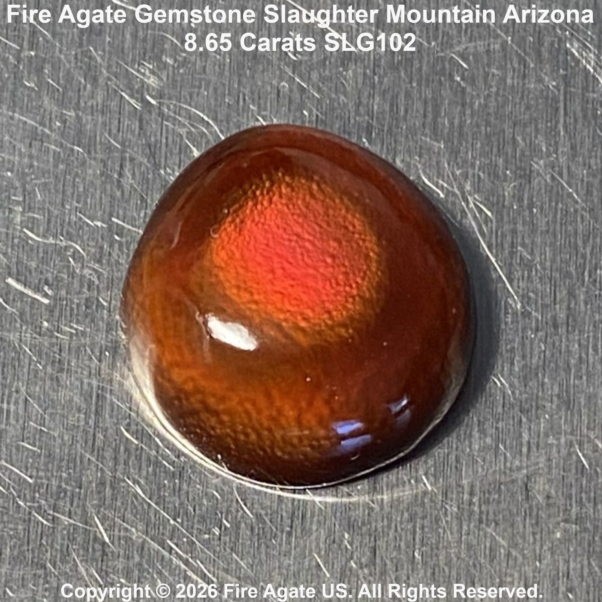 A 8.65 carat fire agate gemstone with a vibrant orange-red center and dark brown outer edges, displayed on a brushed metal surface with text overlays.