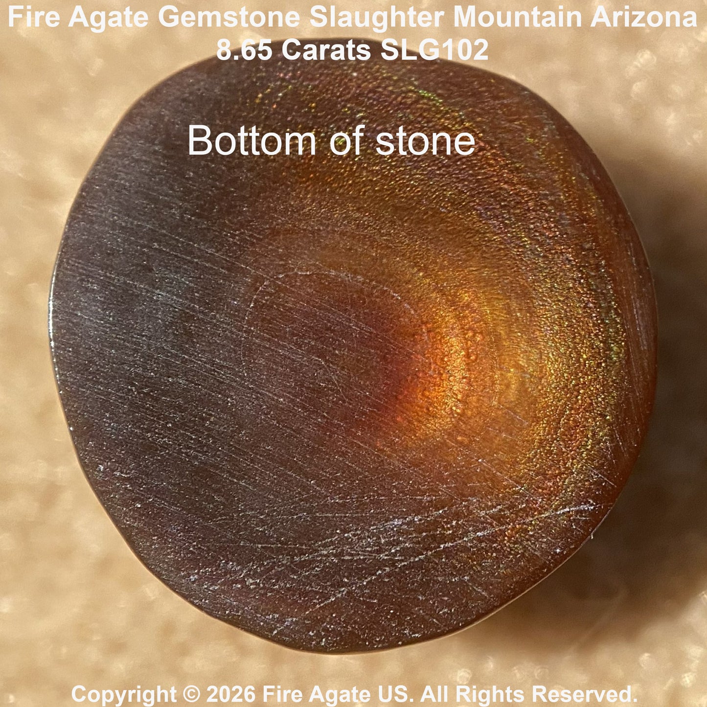 A close-up of the bottom face of a fire agate gemstone, showing a polished circular surface with a dark brown base and warm coppery-orange iridescent play-of-color. White text overlays read 'Bottom of stone' and 'Fire Agate Gemstone Slaughter Mountain Arizona'.
