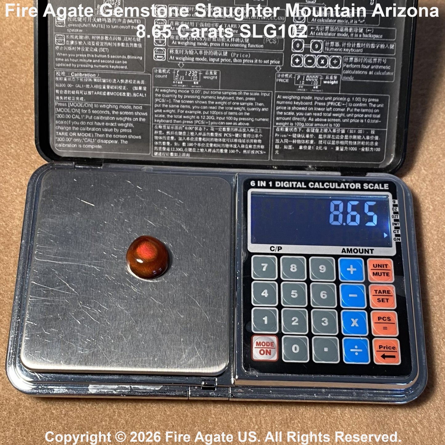 A small digital scale shown open on a tan surface. A round brown gemstone is placed on the weighing platform, and the scale reads 8.65 carats.