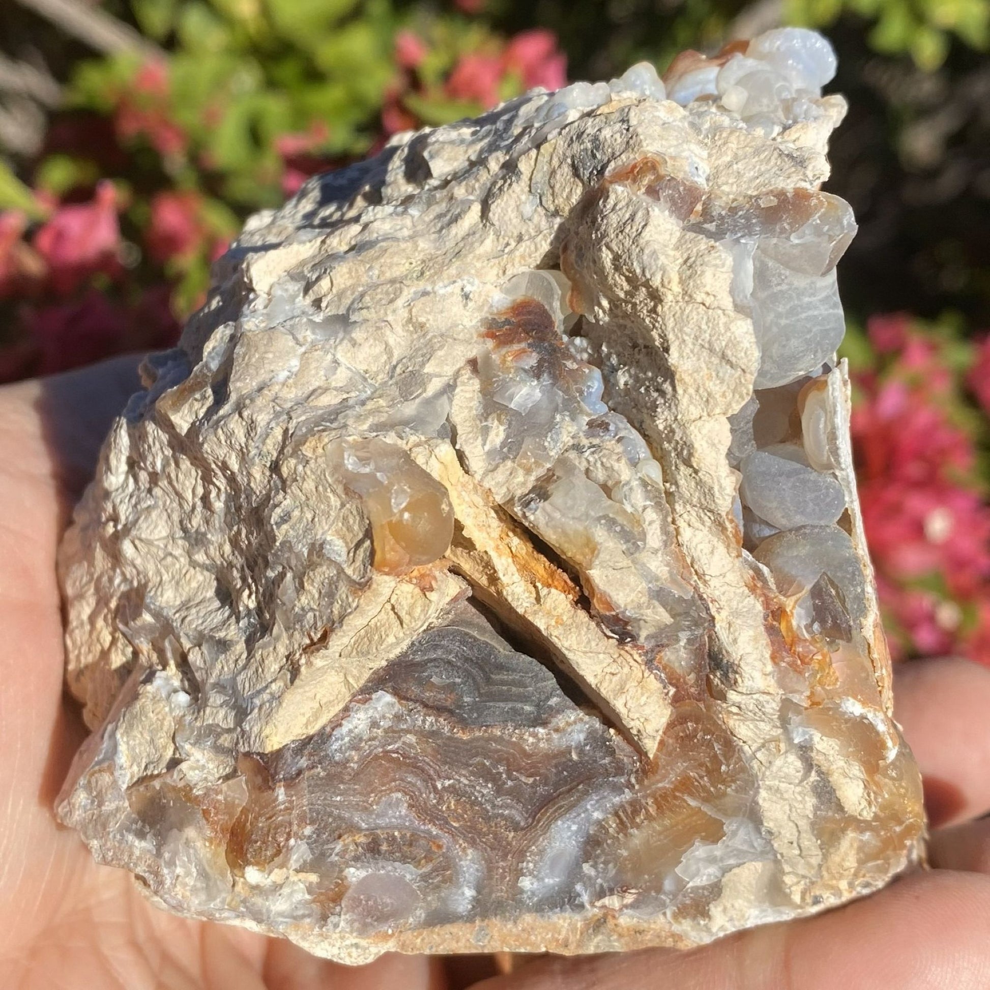 Close-up of a rough crystal rock held in hand with blurred pink flowers in the background