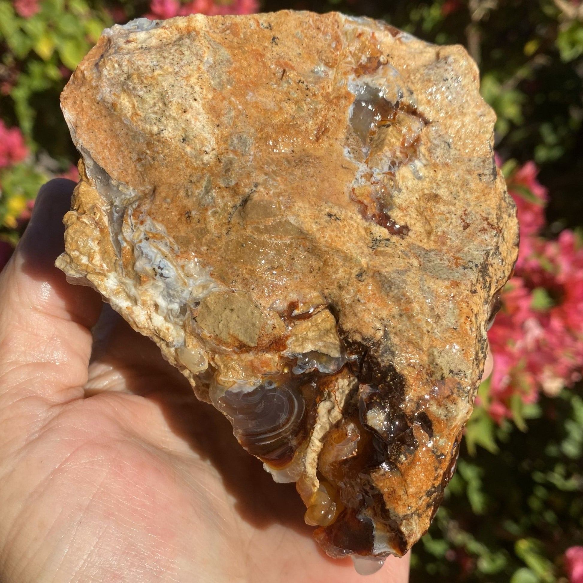 Hand holding a rough-hewn stone with a natural, earthy texture against a blurred floral background.