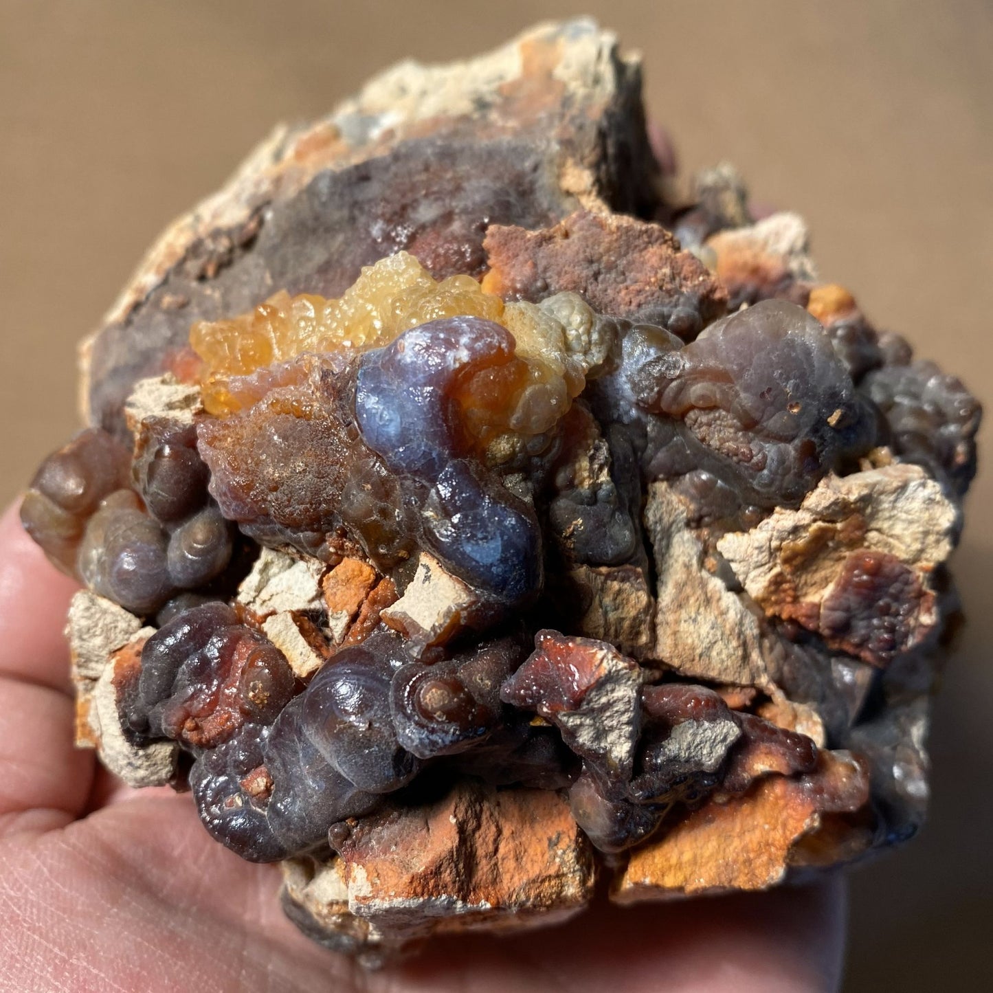 Close-up of a hand holding a piece of high grade fire agate rough with visible minerals
