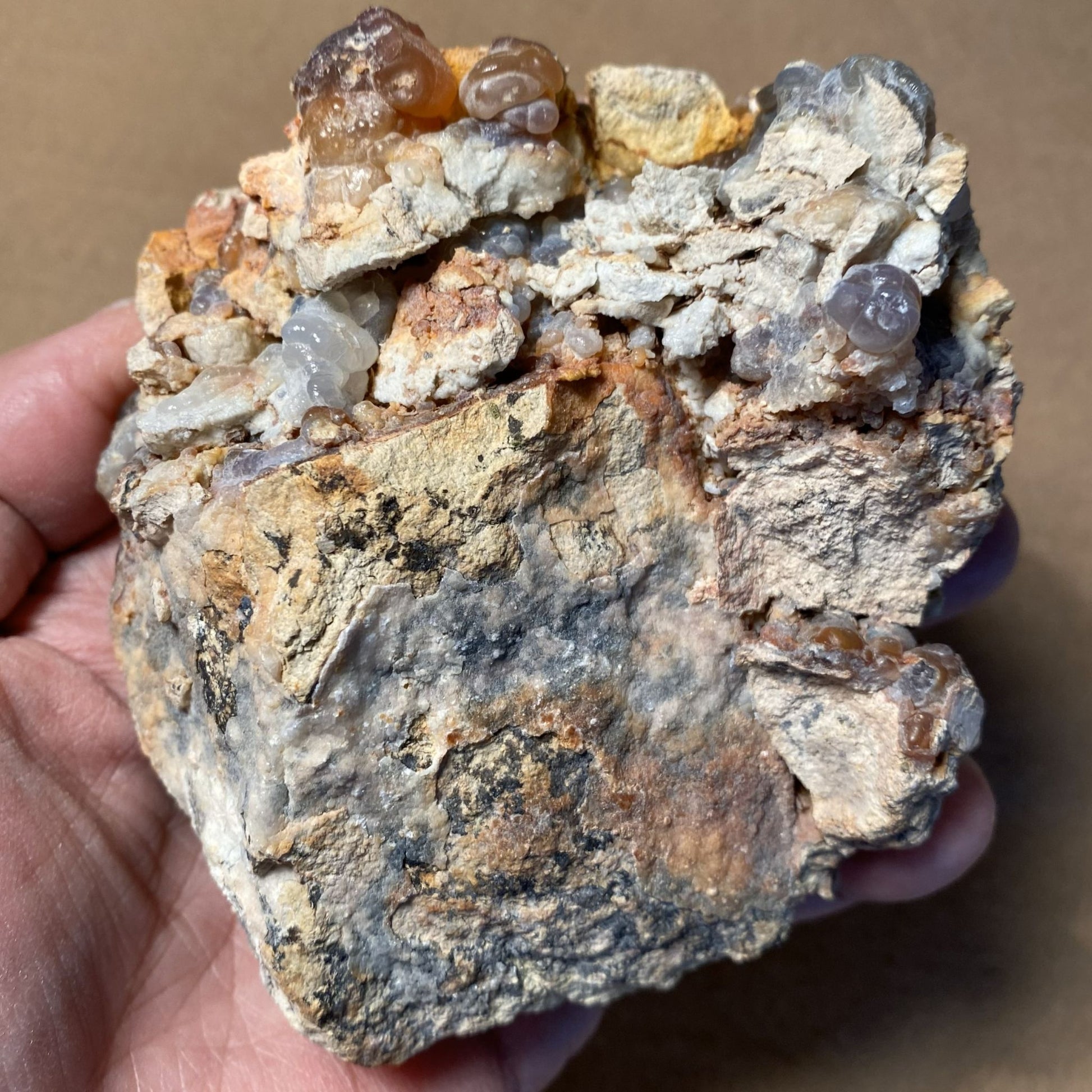 Hand holding a rough mineral rock with visible crystals against a brown background