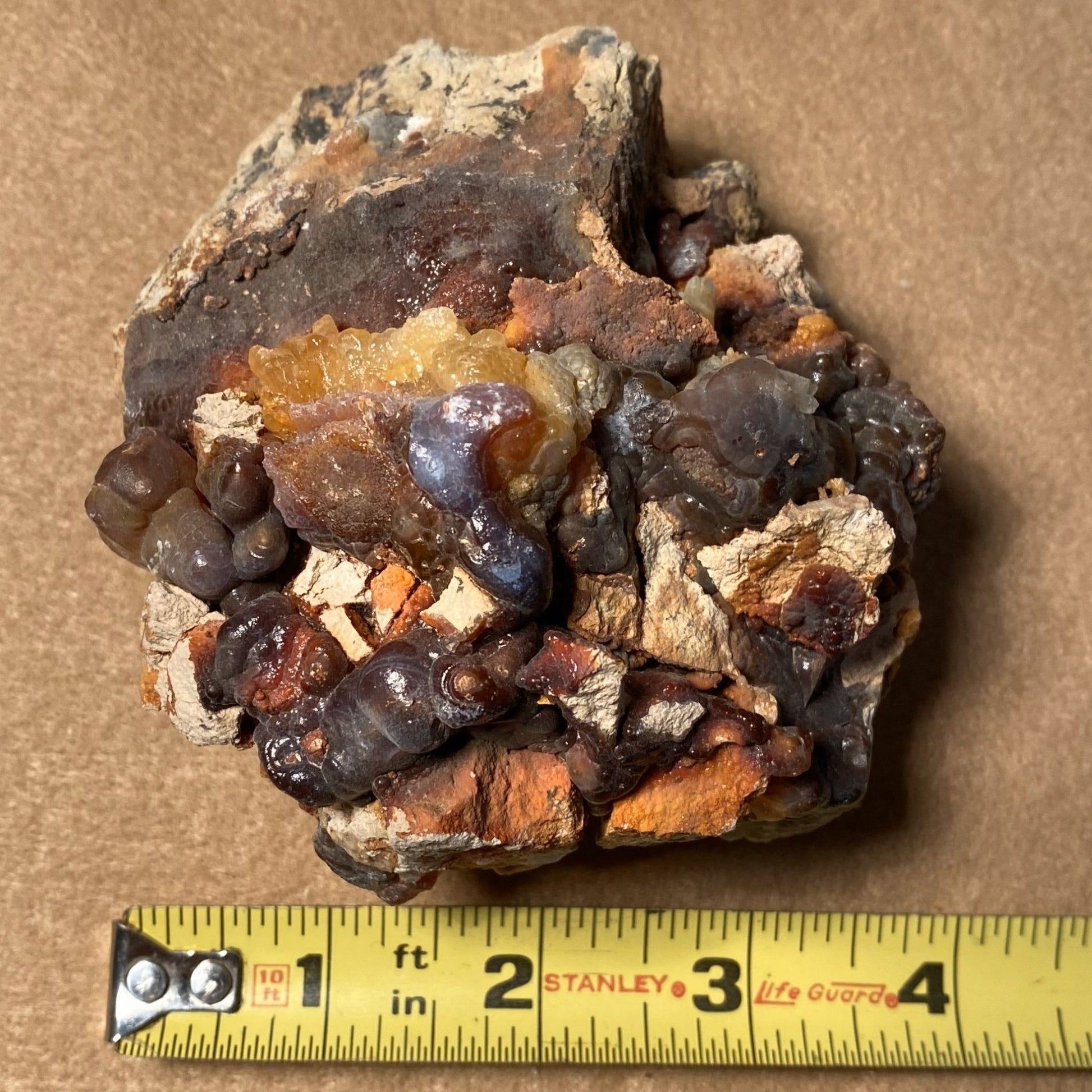 Fire Agate Mineral sample from Slaughter Mountain Arizona with a Stanley measuring tape for scale on a brown background