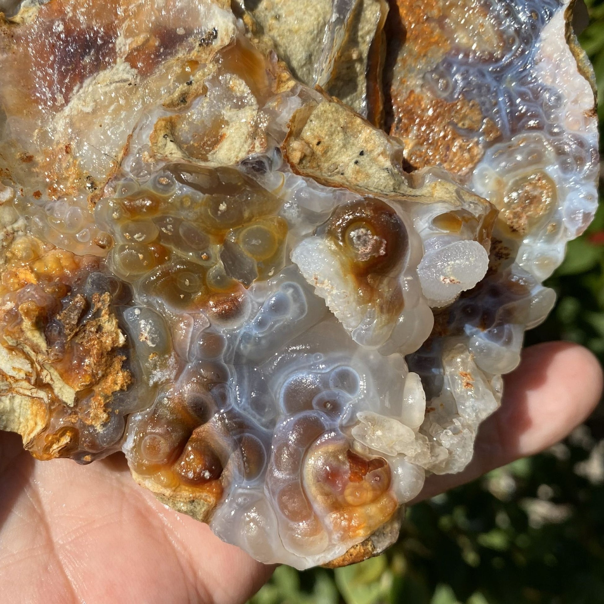 Close-up of a hand holding a translucent fire agate crystal with brown and orange hues.