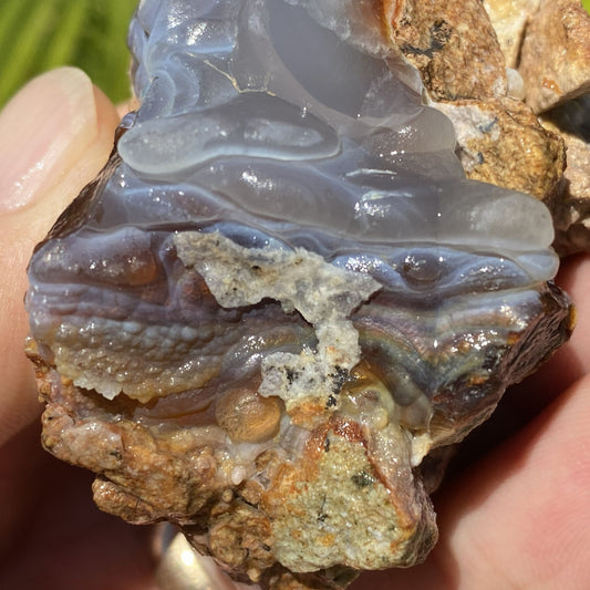 Close-up of a hand holding a piece of Slaughter Mountain fire agate rough with a natural rock background