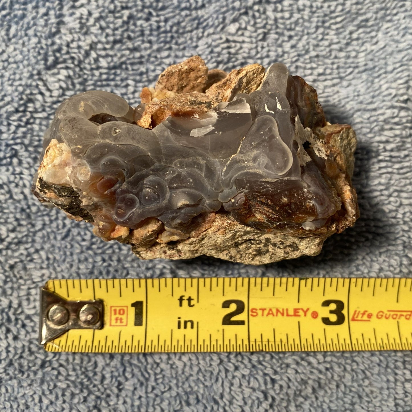 Mineral sample with a measuring tape for scale on a textured gray background