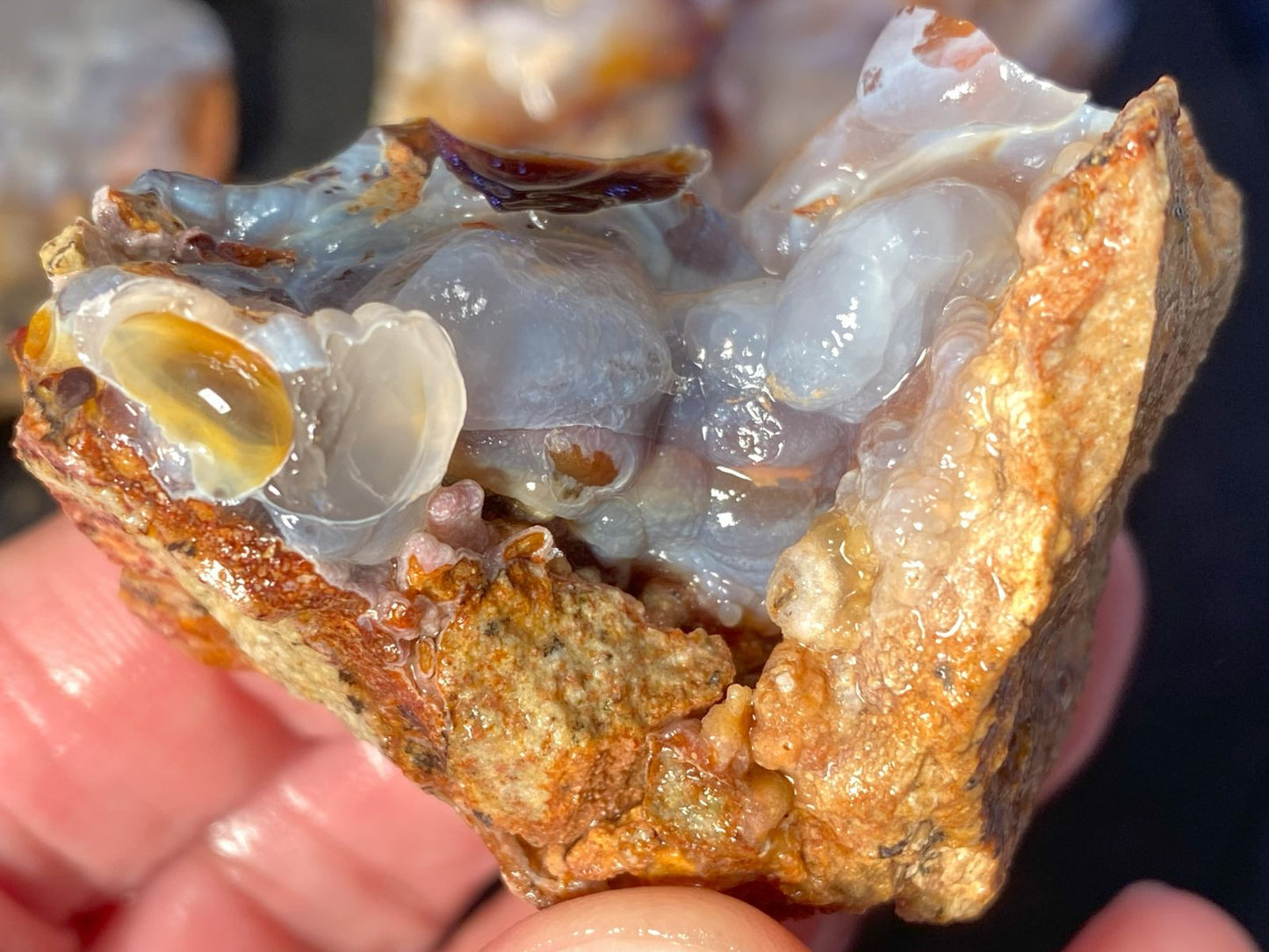 Close-up of a piece of High Grade Slaughter Mountain Fire Agate Rough, held by a hand against a dark background.