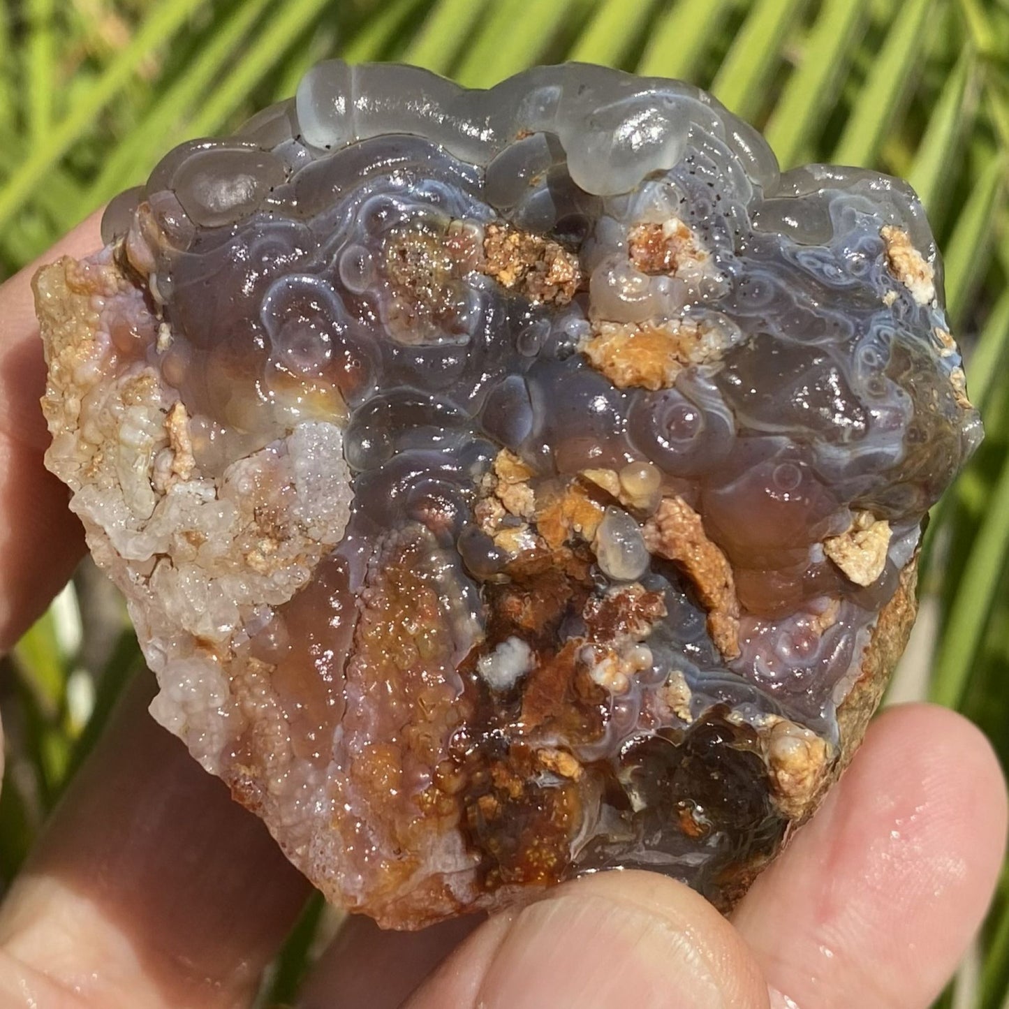 Close-up of a hand holding a crystal rock with a natural background