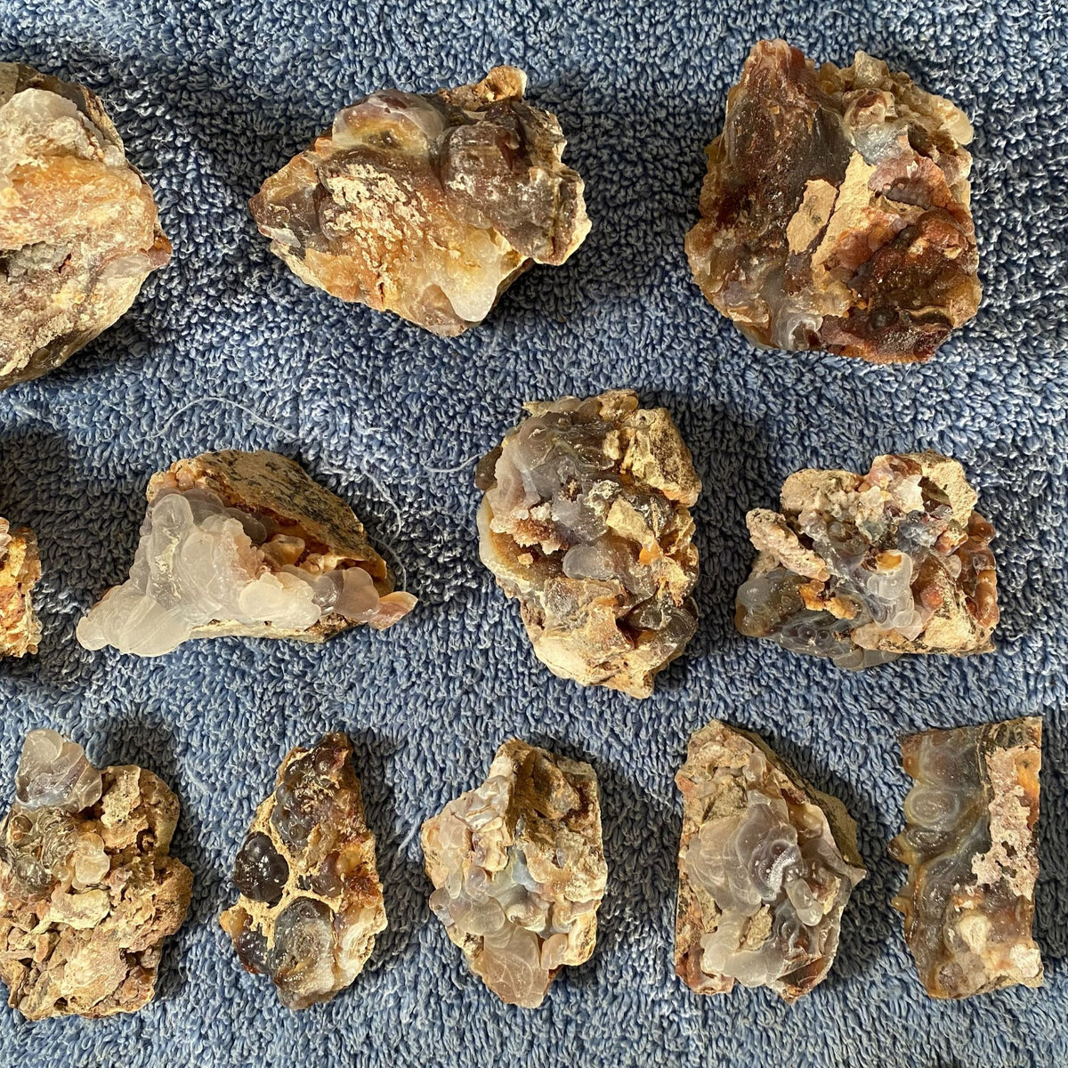 Multiple rough, raw fire agate crystal clusters with natural matrix, displayed on a textured blue towel background.